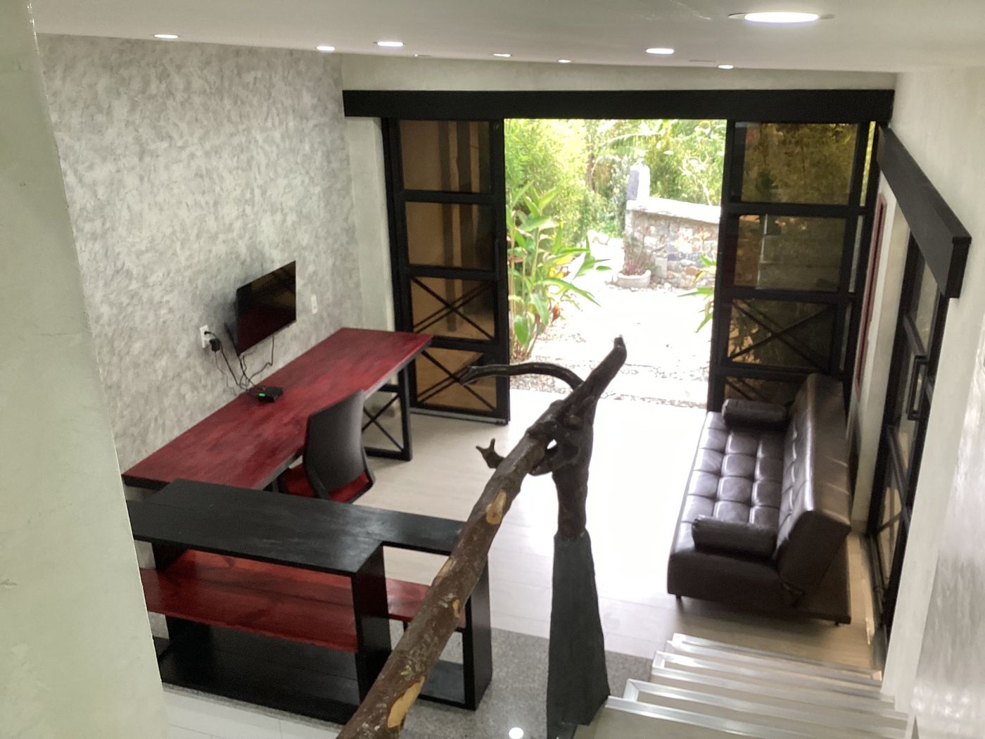 Sala con escritorio, sofá y puertas abiertas al jardín